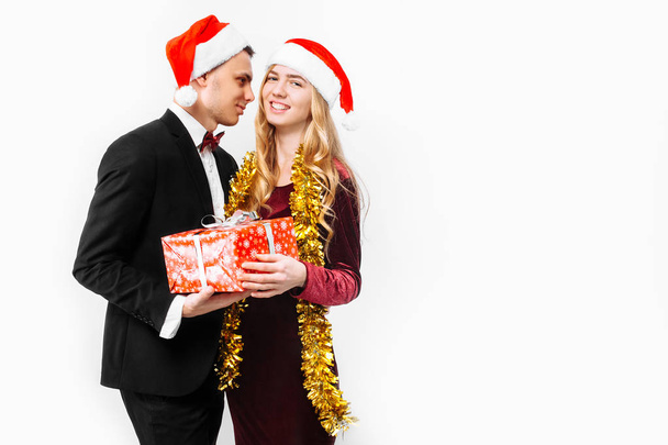 An elegant pair of lovers in Santa Claus hats celebrating the New Year and giving each other Christmas presents. on a white background - Foto, Imagem