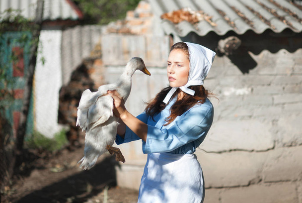 A woman in a village dressed in country style is holding a goose. Shooting in retro style. - Valokuva, kuva