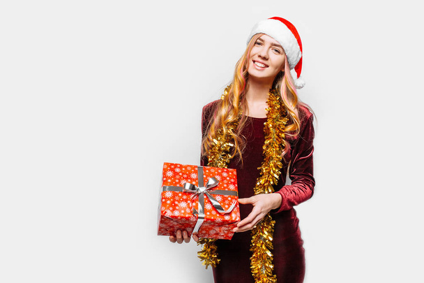 Beautiful girl in the hat of Santa Claus, in her hands a Christmas gift. On a white background - Photo, Image