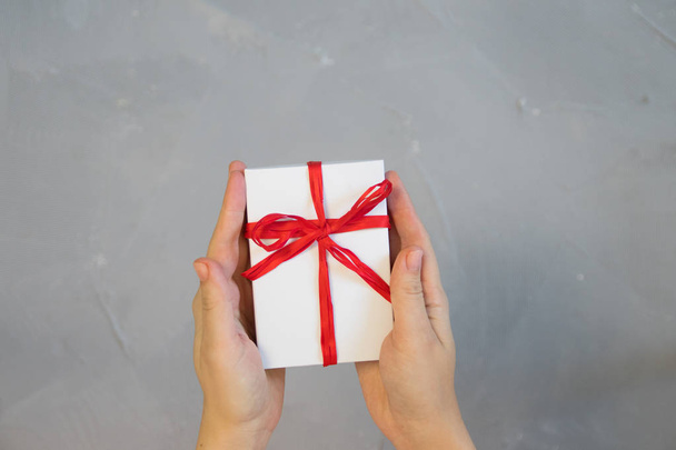 Woman hands holding present box with red bow on pastel pink background with multicolored confetti. Flat lay style. - Φωτογραφία, εικόνα