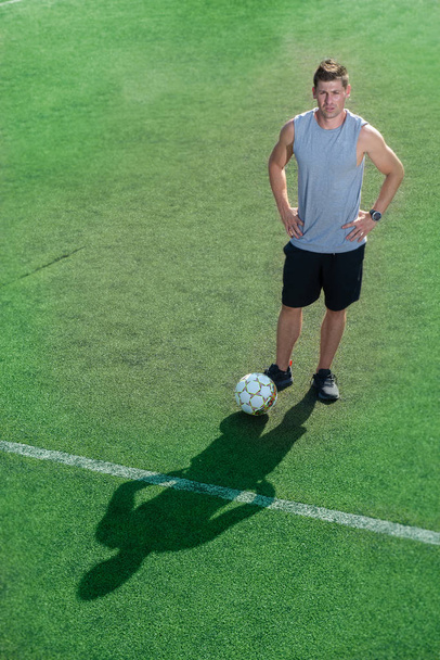 Fotbalový obránce stojící v zeleném poli usmívající se drží jeho míček - Fotografie, Obrázek