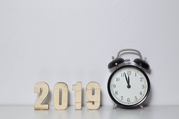Feliz Año Nuevo concepto con despertador y número de madera 2019 en fondo de pared blanca, Copiar espacio
. - Foto, Imagen