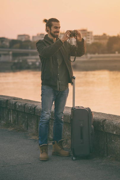 Handsome modern businessman with suitcase enjoys photographing city.Toned image - Foto, Bild
