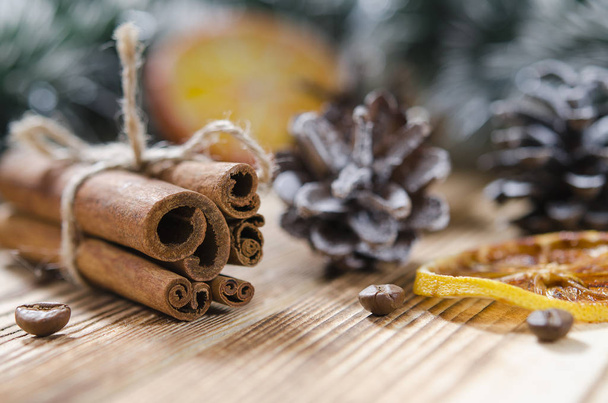 Рождественская открытка: корица и ломтик лимона лежат на коричневом деревянном фоне рядом с сосновыми шишками
 - Фото, изображение