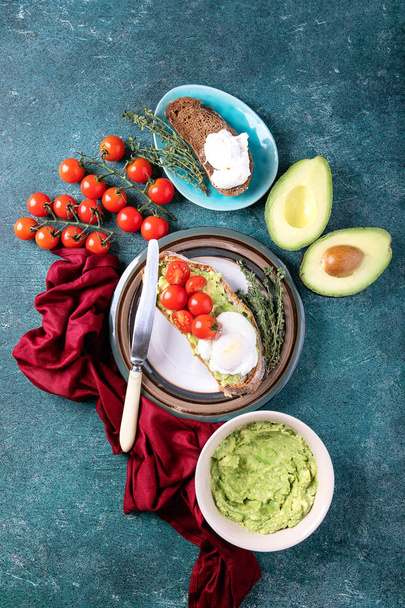 Smashed avocado toast with poached egg served with herbs and tomatoes and guacamole over a green stone background. Top view - Fotografie, Obrázek