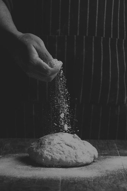 Flour is sprinkled over a ball of dough on wooden board by hand in artistic conversion - Foto, Imagen