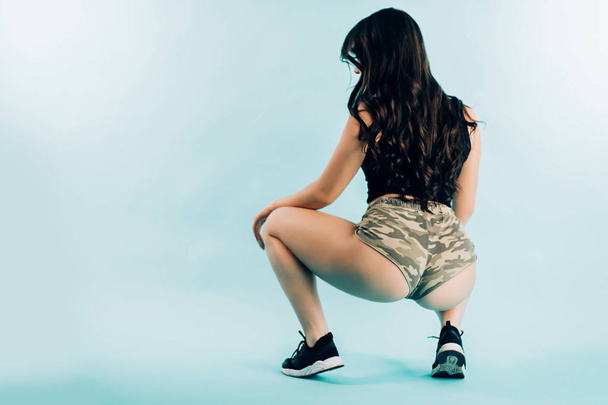 Attractive sexy brunette girl dancing booty dance in the studio sitting on blue background with copy space. - Фото, зображення