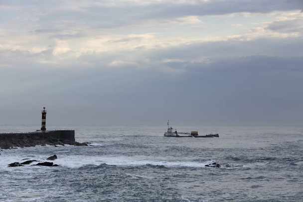 Муди видит корабль, дренаж, покидает устье реки после дноуглубления в конце дня. Северная Португалия
. - Фото, изображение