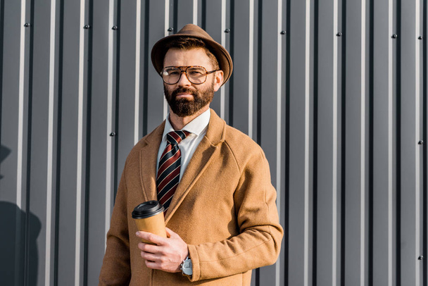 handsome bearded businessman holding coffee to go and looking at camera - Fotografie, Obrázek