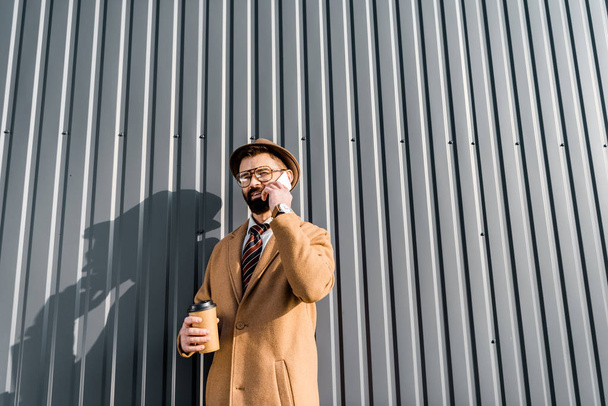 vista de bajo ángulo del hombre de negocios hablando en el teléfono inteligente y la celebración de café para llevar
 - Foto, imagen