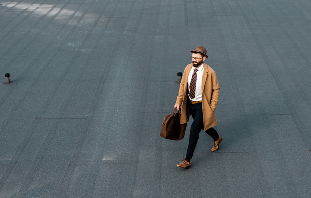 handsome bearded businessman with hat and bag walking on roof - Foto, imagen