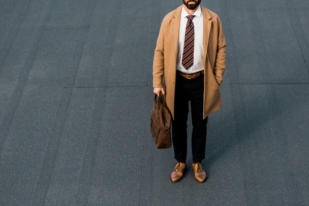 cropped view of bearded businessman standing with leather brown bag - Fotó, kép