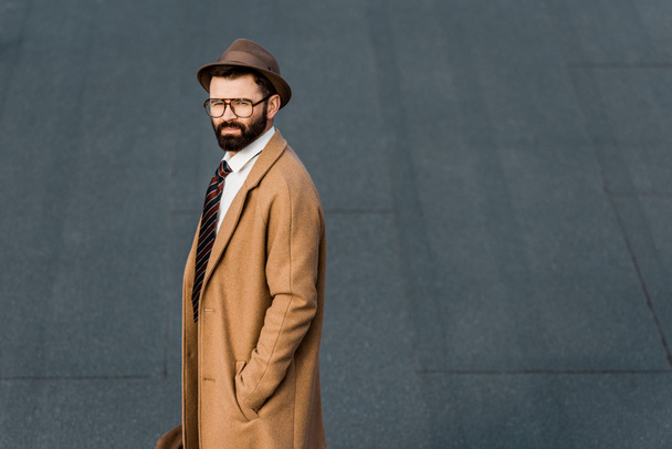 side view of bearded businessman standing in coat with hand in pocket - 写真・画像