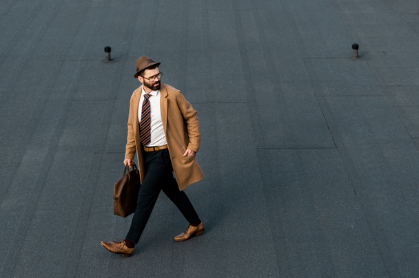 bearded businessman in coat and hat walking with hand in pocket - 写真・画像