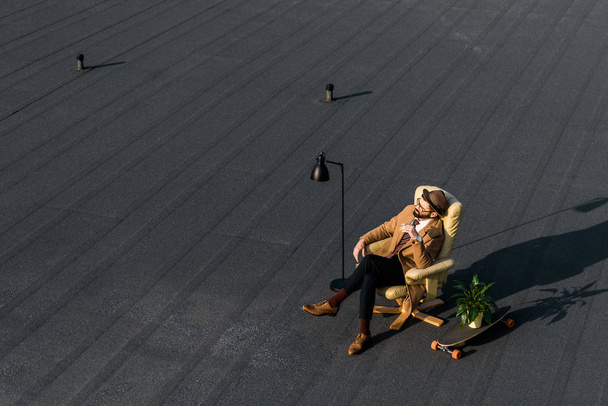 volwassen zakenman rusten in fauteuil met sigaret op dak  - Foto, afbeelding