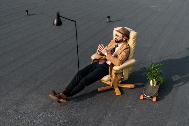 hombre de negocios guapo de abrigo beige sentado en sillón en el techo
 - Foto, imagen