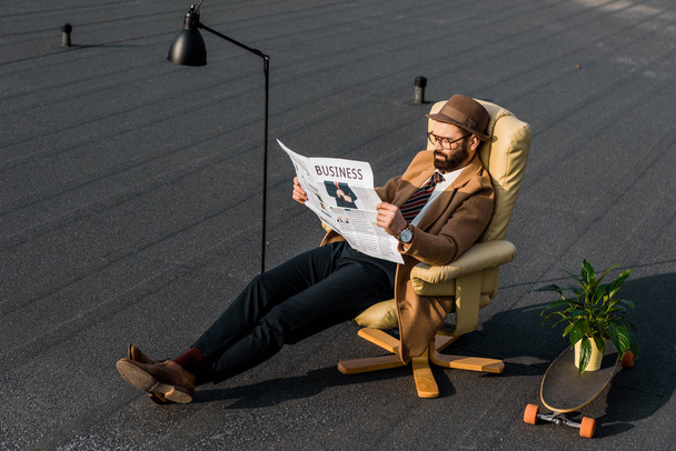 bearded man in coat reading business newspaper in armchair - Fotó, kép