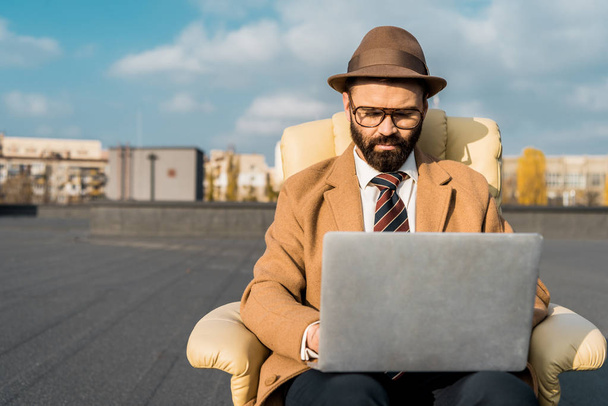 selective focus of businessman in armchair using laptop on roof  - Photo, Image