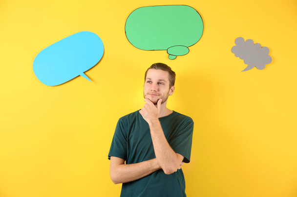 Thoughtful young man and blank speech bubbles on color background - Photo, Image