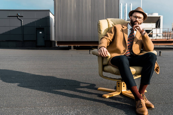 handsome adult businessman sitting in armchair on roof  - Valokuva, kuva