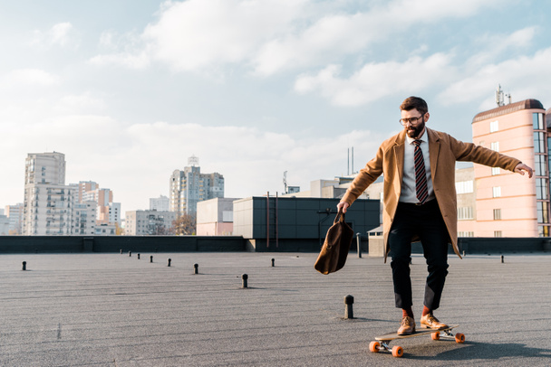 Handsome businessman riding on penny board on roof  - Valokuva, kuva