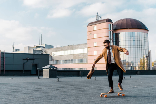 bearded businessman riding on penny board with bag in hand  - Fotó, kép
