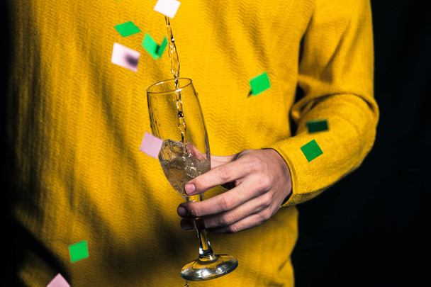 Young man in yellow sweater pours champagne in a glass - Foto, afbeelding