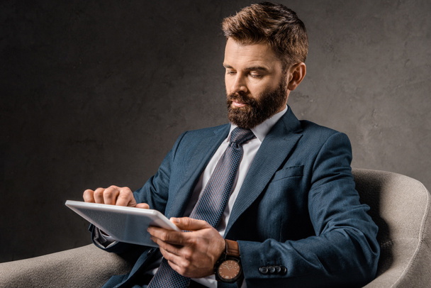 bearded businessman using digital device while sitting in armchair  - 写真・画像