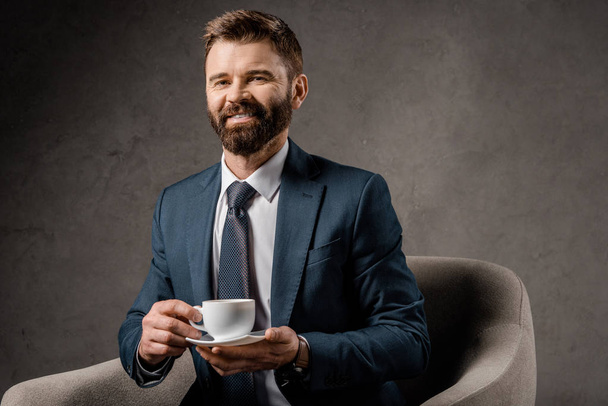 smiling businessman sitting in armchair with cup of coffee  - Zdjęcie, obraz