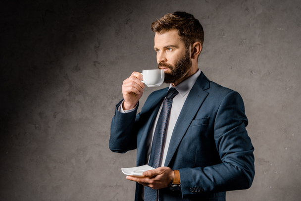 handsome businessman drinking coffee and holding saucer - Fotoğraf, Görsel