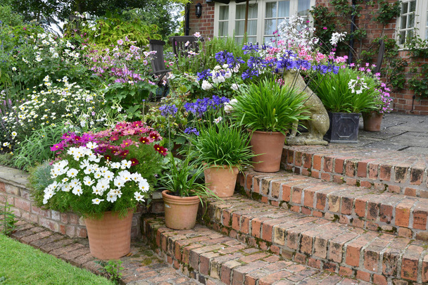 Colorida terraza jardín con macizos de flores mixtas y contenedores plantados que hacen una exhibición muy atractiva frente a una casa de campo
 - Foto, Imagen