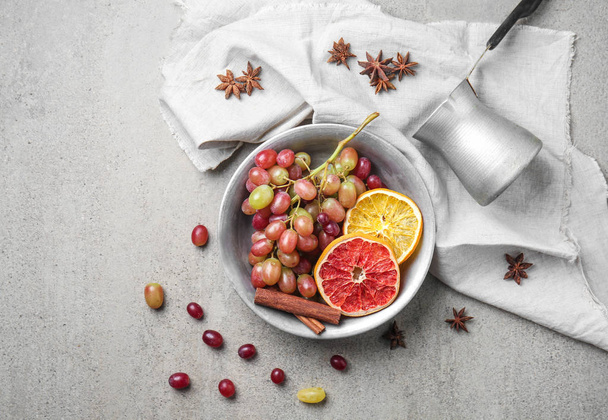 Bowl with sweet grapes, dried citrus slices and spices on grey table - Photo, Image