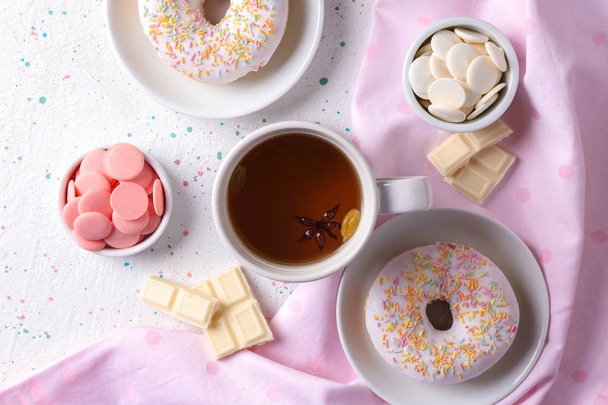 Сладкие пончики, шоколадные чипсы и чашка чая на столе, вид сверху
 - Фото, изображение