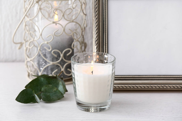 Burning candle near photo frame on table - Фото, изображение
