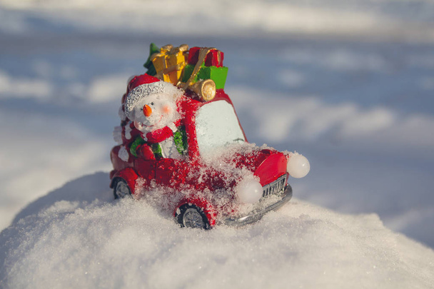 Vrolijk speelgoed sneeuwpop op een auto draagt geschenken. Nieuwjaar - Foto, afbeelding