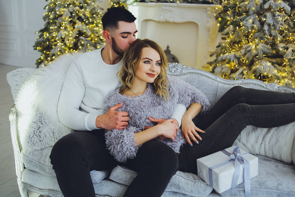 A couple in love gently smiling at each other, sitting on the sofa near the Christmas, New Year tree - Foto, Imagen
