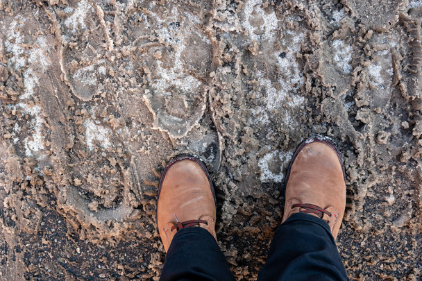 Mans feet in winter boots on dirty snow in the streets. - 写真・画像