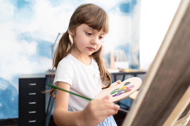 Portrait of a beautiful liitle girl draw and paint in canvas at her home.Concept of early childhood education, happy family, parenting - Foto, Imagen