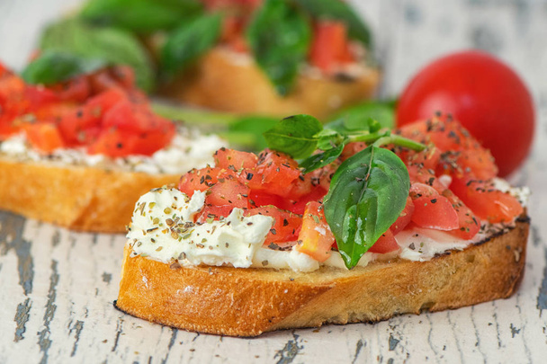 Geleneksel İtalyan domates bruschetta baharat ve fesleğen ile ışık ahşap arka plan üzerinde tost. Yakın çekim. - Fotoğraf, Görsel