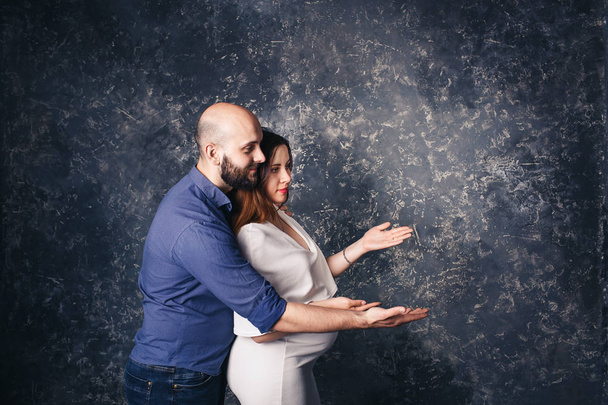 Young pregnant couple holding copyspace on the palm. - Фото, изображение