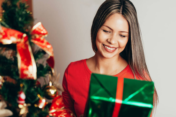 Smiling young woman with christmas present box near christmas tree - Fotó, kép