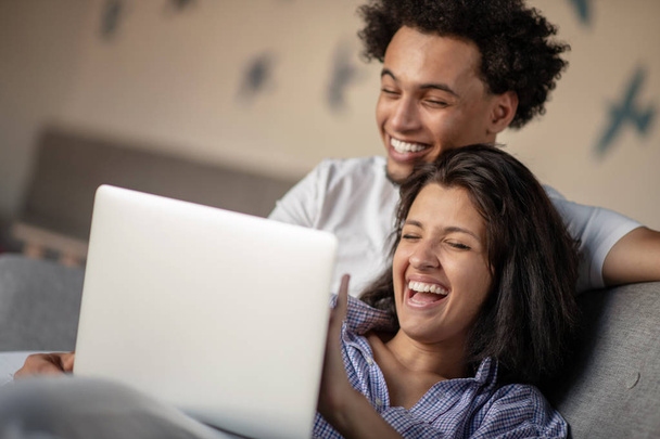 Cheerful happy African American young marriage laughing while watching movie on laptop computer at home interior. - Foto, afbeelding