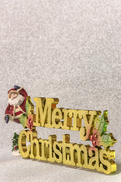 Legrační figurka Santa Claus na pozadí třpytky stříbrné sníh s zlatá slova Veselé Vánoce a vánoční strom ornament. - Fotografie, Obrázek