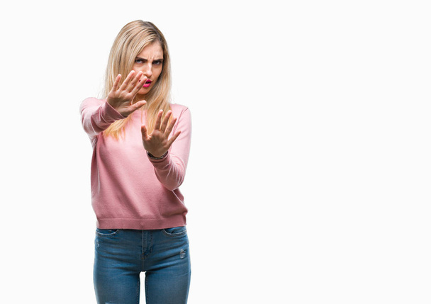 Young beautiful blonde woman wearing pink winter sweater over isolated background afraid and terrified with fear expression stop gesture with hands, shouting in shock. Panic concept. - Photo, Image