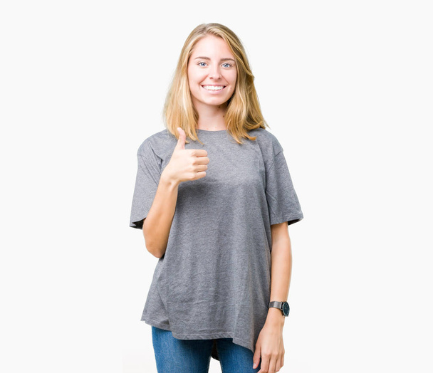 Красива молода жінка, одягнена в надлишкову футболку над ізольованим тлом, робить щасливі великі пальці вгору жестом рукою. Затвердження виразу, який показує успіх фотоапарата
. - Фото, зображення