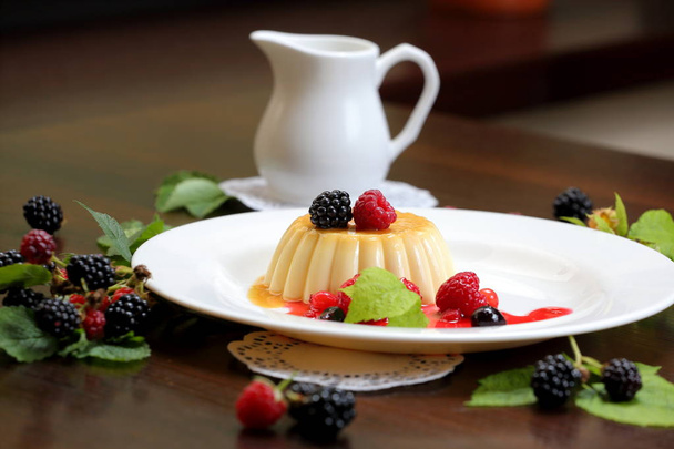 budín de vainilla con bayas y crema en un plato blanco de cerca
 - Foto, imagen