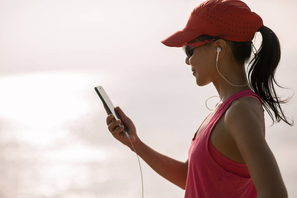 Fitness sportswoman listening music with mobile phone on sunny coast - Photo, image