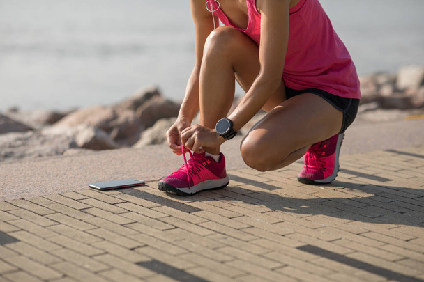 Fitness sportswoman tying shoelace on sunny coast - Foto, Bild