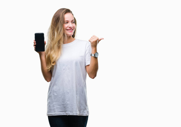 Молода красива блондинка показує екран смартфона над ізольованим фоном, вказуючи і показуючи з великим пальцем в сторону з щасливим обличчям посміхаючись
 - Фото, зображення