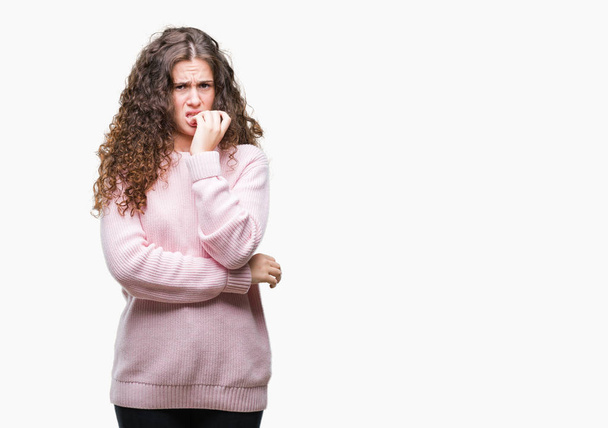 美しいブルネット毛少女不安や両手の爪を噛んで口の中で緊張を探して孤立の背景にピンク冬セーターを着ています。不安の問題. - 写真・画像